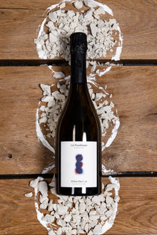 Eine Flasche des Winzerchampagners Les Pinailleuses von Hélène Charbaut wird umrahmt von Kalk- und Kreidesteinen die den Boden repräsentieren sollen auf dem die Trauben wachsen.